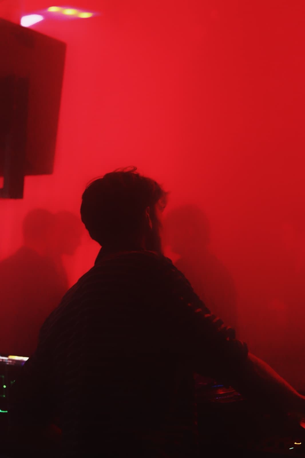 DJ silhouetted in deep red haze behind the decks