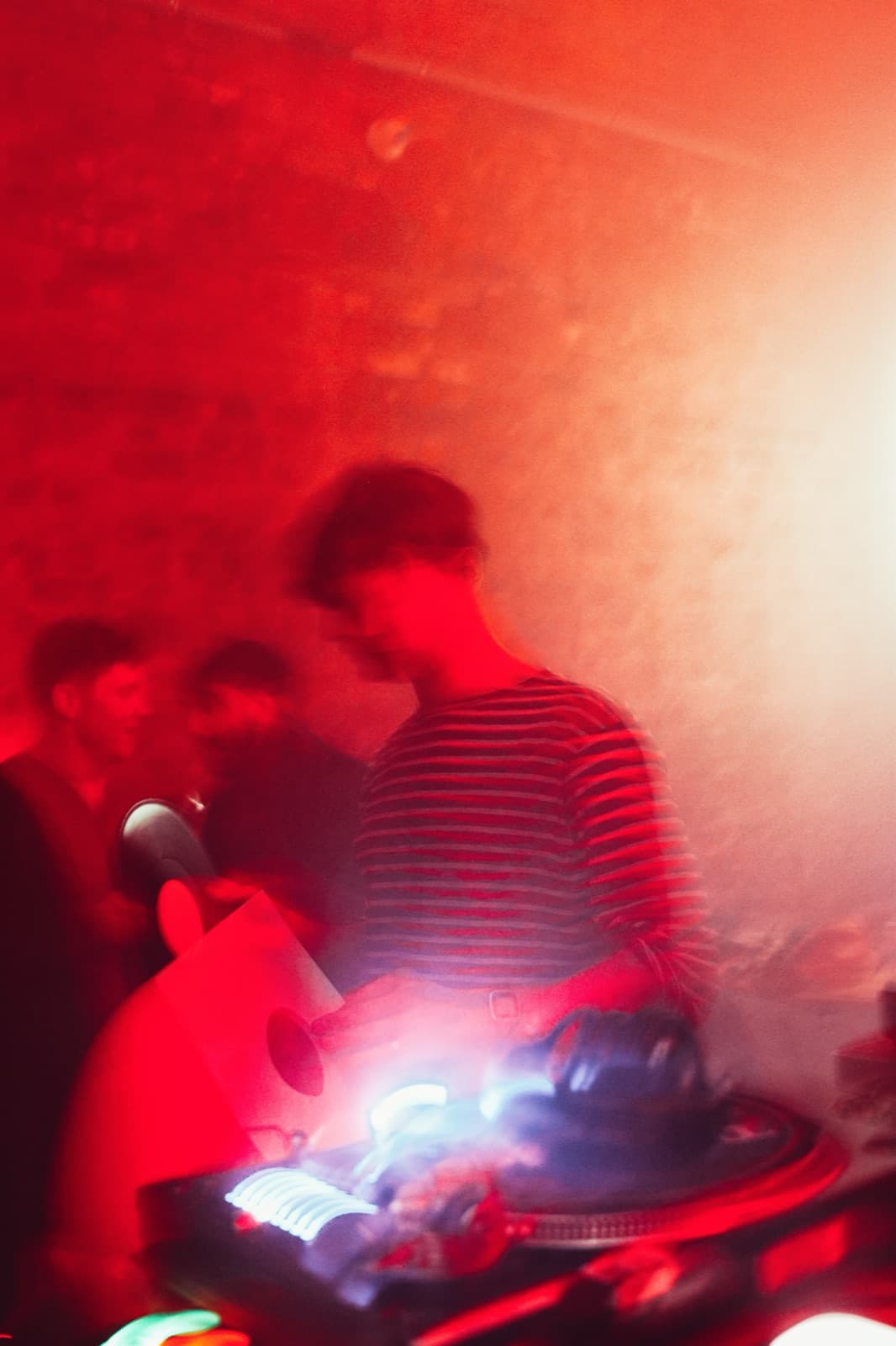 DJ in a striped top at the turntables amid motion blur and red haze
