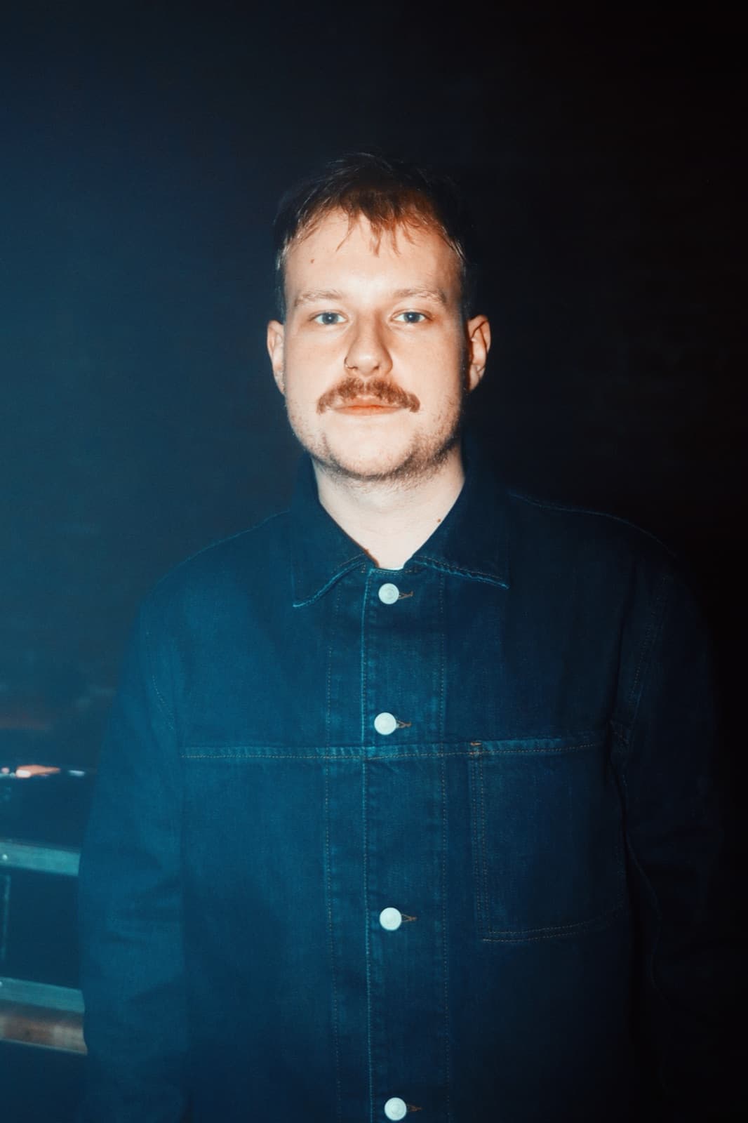 Portrait of a person in a denim jacket lit warm against the dark
