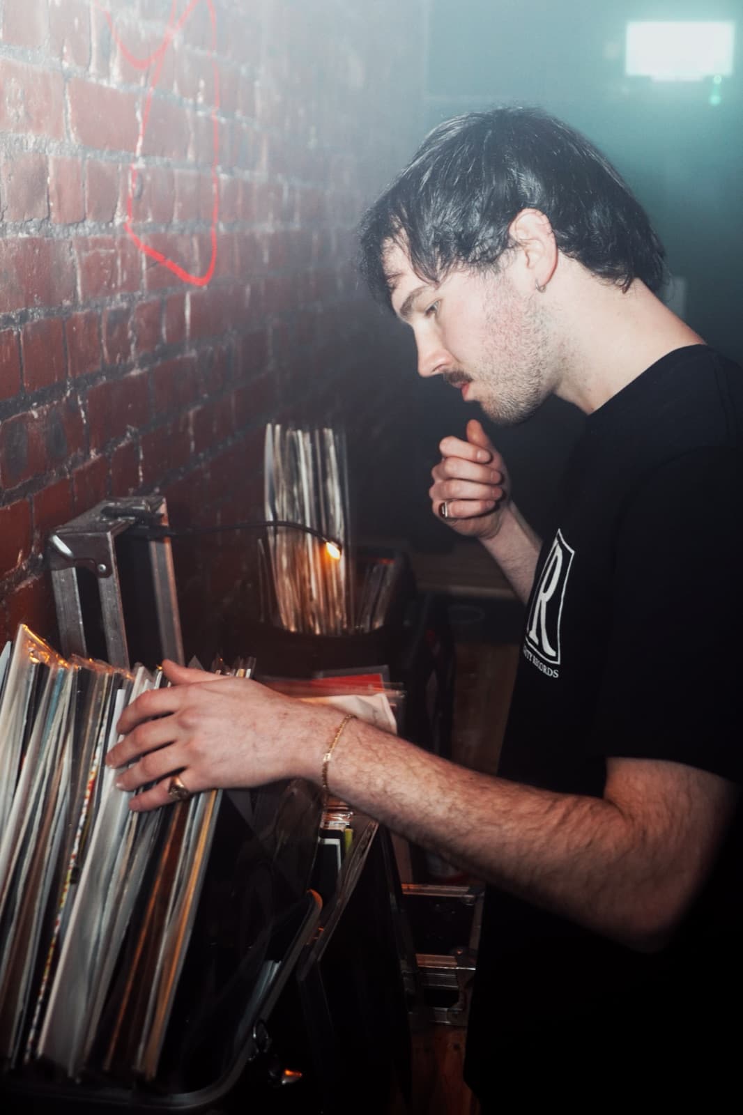 DJ digging through a vinyl crate against an exposed brick wall