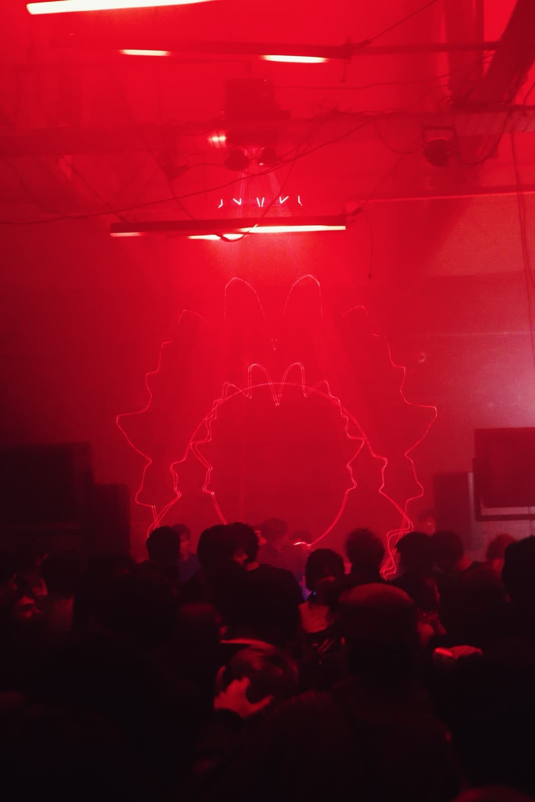Red laser art forming a circular burst over the crowd in a warehouse